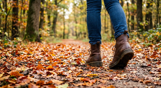 Low angle photograph from behind of a person in denim jeans and brown leather lace-up boots walking away on a leaf-covered forest trail. Large text overlaid in the upper half reads 'A Walk in the Woods'.