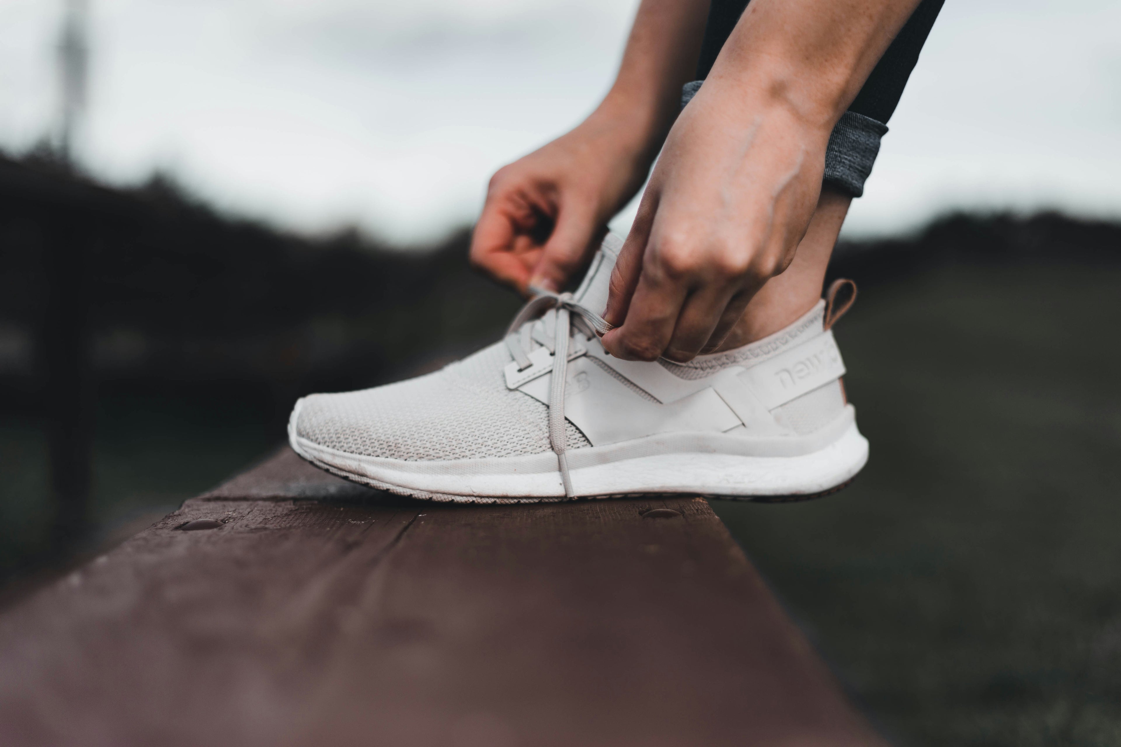  A person preparing for a workout by securely tying their white athletic shoe laces while sitting outside. 
